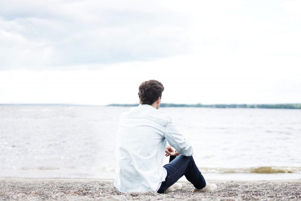Man sitting on the shore and looking out at the water.