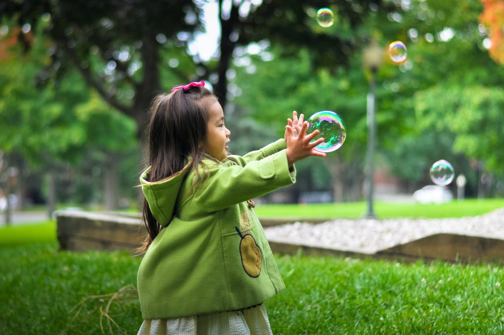 Young girl outside with her hands about to catch a bubble.