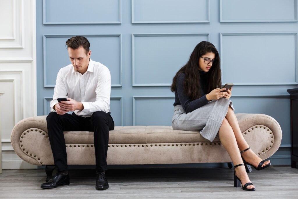 smart businessman and young businesswoman keep social distancing while using smartphone