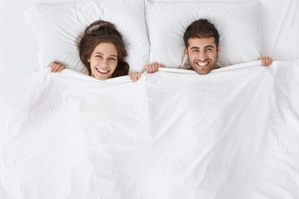 Top view of heads of happy lovely couple lying in bed and smiling broadly after good sex. Lovers enj