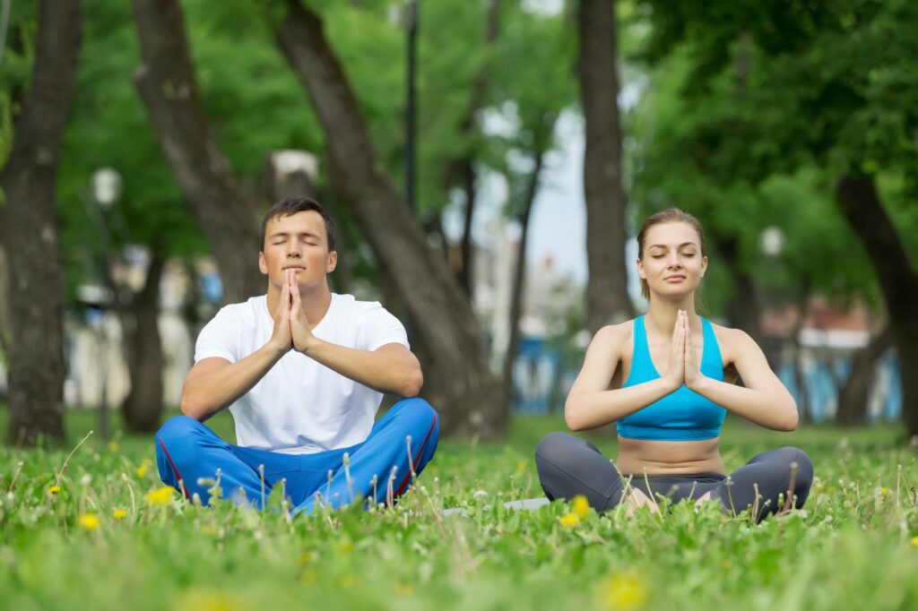 Young couple meditating on green grass