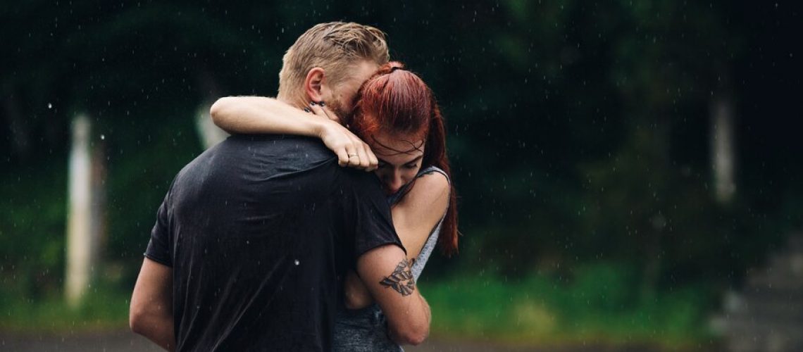 Intimate couple hugging outside while raining