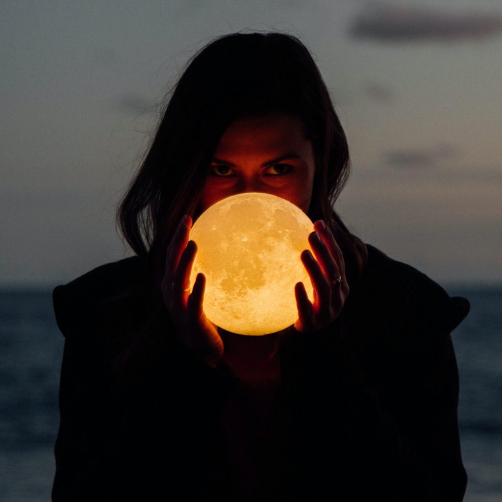 Woman holding illuminated moon in hands to represent Women's Moon Circle.