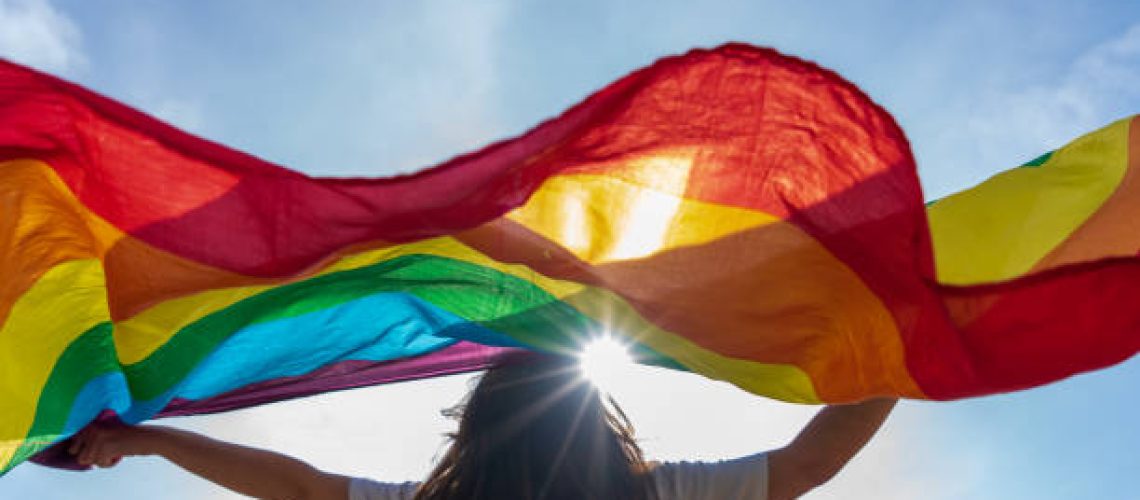 Picture of a young woman waving lgbti flag under the sky