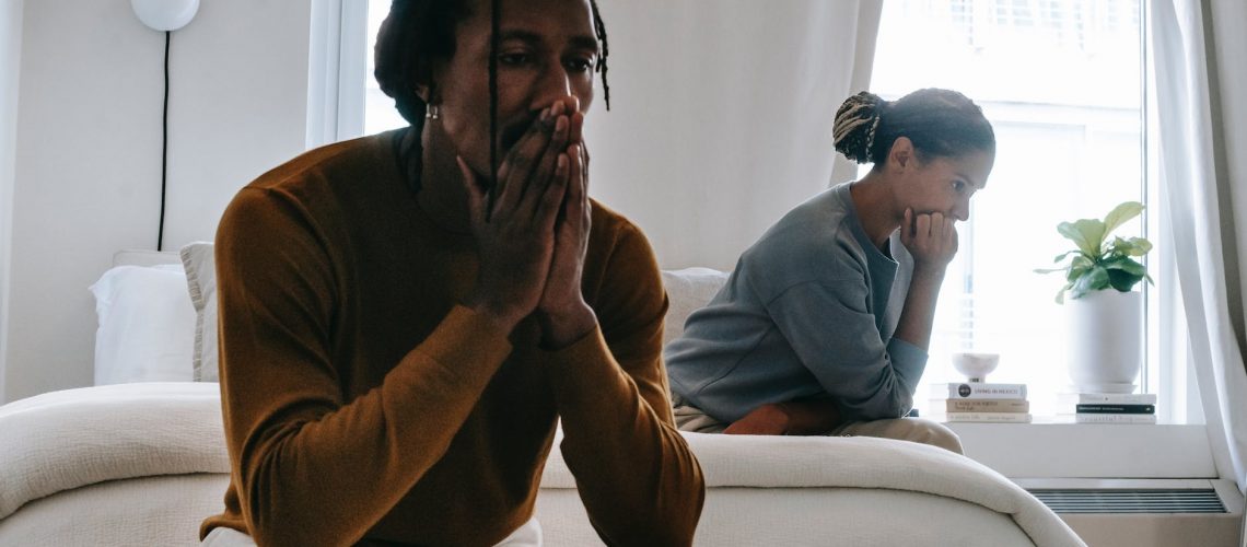 unhappy black couple sitting on bed after having argument
